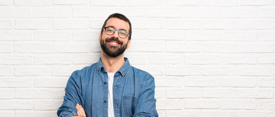 Handsome man with beard over white brick wall with glasses and happy