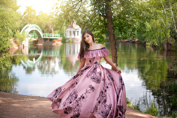 Beautiful young woman in a dress of the 19th century by the pond. Romantic girl in the park.