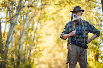 Fototapeta premium Bearded caucasian hunter wearing cowboy hat in search of trophy in autumn forest. Stand looking for prey in hunting period, autumn season open.
