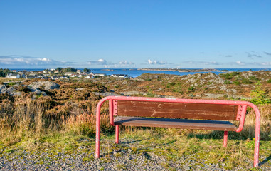 Fototapeta na wymiar red bench standing on a mountain with a view of the town against the blue sky on a warm sunny autumn day