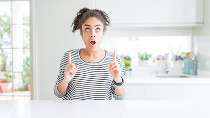 Beautiful african american woman with afro hair wearing casual striped sweater amazed and surprised looking up and pointing with fingers and raised arms.