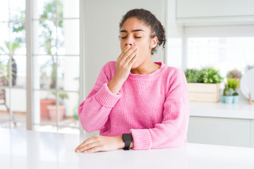 Beautiful african american woman with afro hair wearing casual pink sweater bored yawning tired covering mouth with hand. Restless and sleepiness.