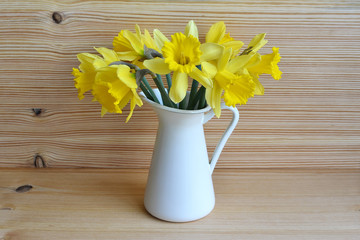 Bouquet of beautiful yellow narcissus in vase on wooden background