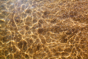 Golden sand under clear sea water and sunlight glow reflection close up top view, yellow sandy beach coast texture below transparent ocean surface background, abstract natural seaside pattern backdrop