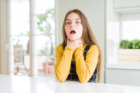 Young beautiful blonde kid girl wearing casual yellow sweater at home shouting suffocate because painful strangle. Health problem. Asphyxiate and suicide concept.