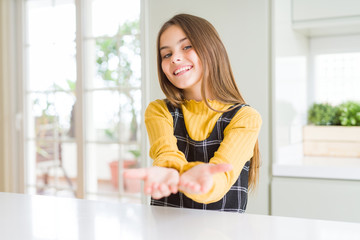 Young beautiful blonde kid girl wearing casual yellow sweater at home Smiling with hands palms together receiving or giving gesture. Hold and protection