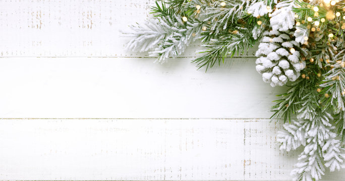 Christmas tree branch and pine cone in snow on a white wooden background. Winter festive concept. Flat lay, copy space.