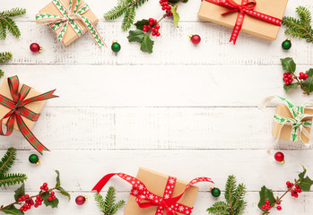 Christmas background with gift boxes, Christmas decorations and branches of holly and fir on white wooden background. Winter festive concept. Flat lay, copy space.