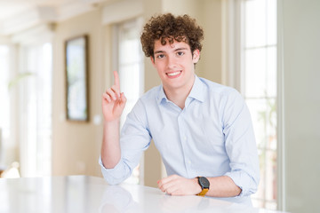 Young business man with curly read head showing and pointing up with finger number one while smiling confident and happy.