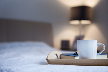 Cup of hot drink and book on bed