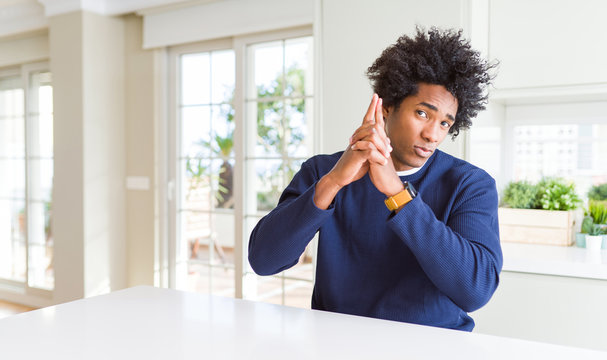 Young african american man wearing casual sweater sitting at home Holding symbolic gun with hand gesture, playing killing shooting weapons, angry face