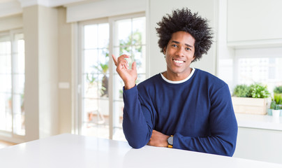 Young african american man wearing casual sweater sitting at home with a big smile on face, pointing with hand finger to the side looking at the camera.