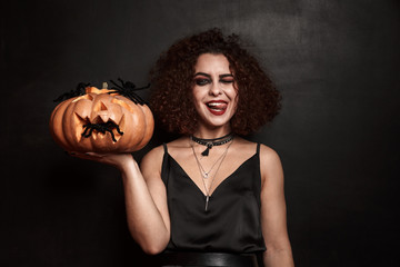 Image of joyful witch girl holding halloween carved pumpkin with spiders
