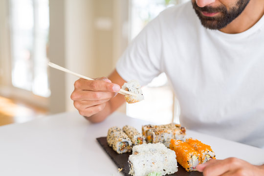 Handsome man smiling happy enjoying eating fresh colorful asian sushi using chopsticks