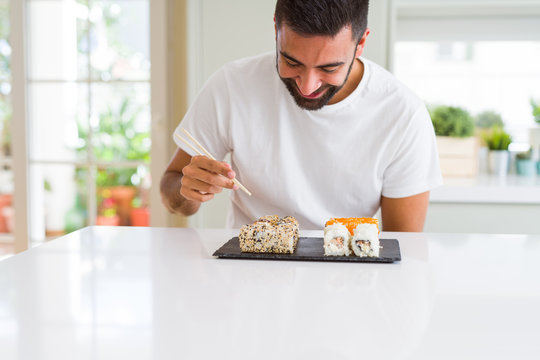 Handsome man smiling happy enjoying eating fresh colorful asian sushi using chopsticks