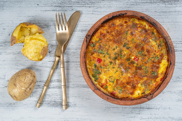 Ceramic bowl with vegetable frittata, simple vegetarian food. Frittata with tomato, pepper, onion and cheese on wooden table, close up. Italian egg omelette