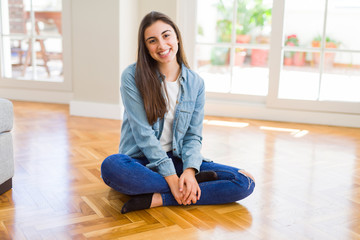 Beautiful young brunette woman smiling cheerful looking at the camera with a big smile on face sitting on the floor at home with sunlight at the background