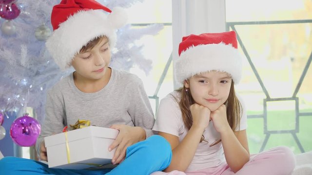 Sweet scene where brother is cheering his upset sister up, giving her new year present, tenderly embracing.