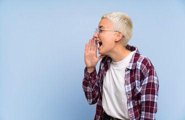 Teenager girl with white short hair over blue wall shouting with mouth wide open