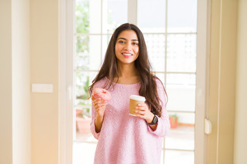 Young worker woman taking a break eating tasty pink donut and drinking a cup of coffee