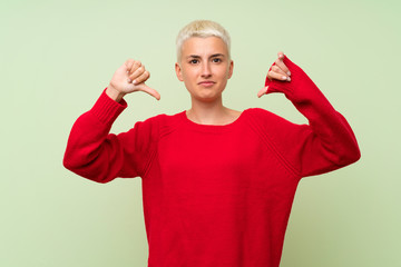 Teenager girl with white short hair over green wall showing thumb down