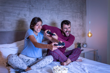 Couple having fun playing video games in bed at night