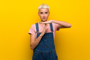 Teenager girl with overalls on yellow background making time out gesture