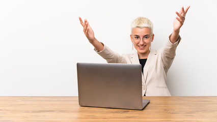 Teenager girl with short hair with a laptop presenting and inviting to come with hand