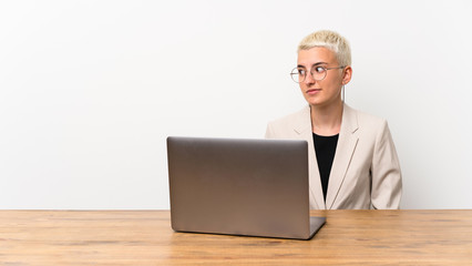 Teenager girl with short hair with a laptop making doubts gesture looking side