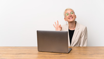 Teenager girl with short hair with a laptop saluting with hand with happy expression