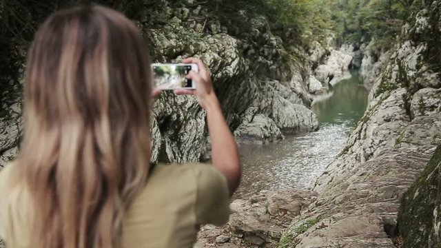 A woman take a picture of a mountain river in a crevice in the rocks
