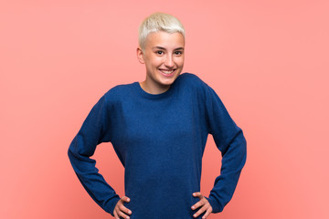 Teenager girl with white short hair over pink wall posing with arms at hip and smiling