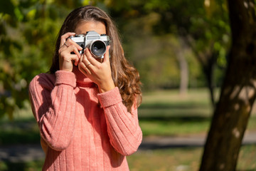 Young brunette woman taking a photo with old style camera outdoor in a park.