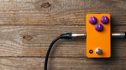 Blank orange guitar pedal with purple knobs and plugged jacks on wooden floor