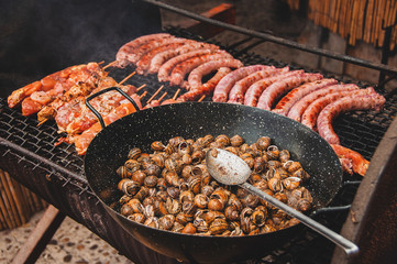 Traditional Mediterranean Snail Recipe and barbecue with sausages and meat on skewers . Tasty and freshly cooked hot snails and meat, smoke is visible.