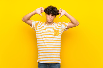 Young man over isolated yellow wall showing thumb down