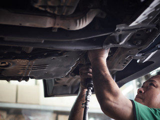 Auto mechanic working underneath car lifting machine at the garage. Auto repair shop, Car service, repair.