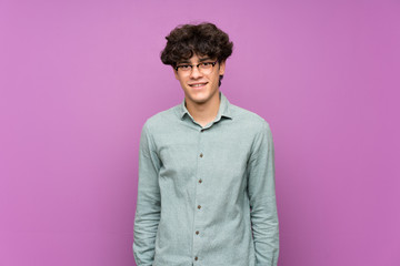 Young man over isolated purple wall with glasses and happy