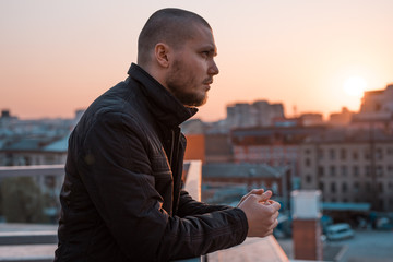 Fototapeta premium young handsome serious man looks away on the background of the city at sunset