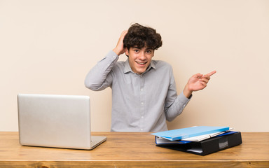 Young student man with a laptop surprised and pointing finger to the side