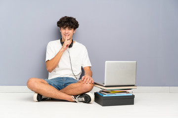 Young man with his laptop sitting one the floor doing silence gesture