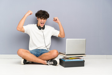 Young man with his laptop sitting one the floor celebrating a victory