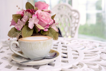 A cup of coffee withe beautiful flowers on whtie table in selective focus on coffee cup, with garden background.