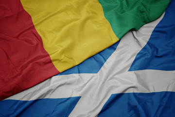 waving colorful flag of scotland and national flag of guinea.