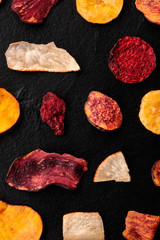 Dried fruit and vegetable chips, shot from above. Healthy vegan snack, an organic food flat lay pattern on a black background