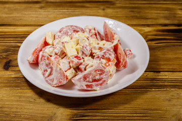 Tasty salad with crab sticks, cheese, tomato and mayonnaise on wooden table