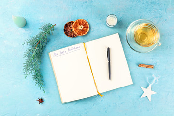 New Year's resolutions, flat lay overhead shot with the handwritten header and a place for text, on a blue background with Christmas decorations and hot tea