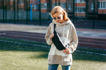 Fototapeta premium Stylish model girl at the city in a grey hoodie and glasses with waist bag