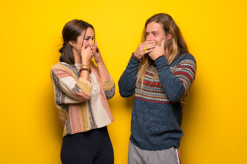 Hippie couple over yellow background covering mouth with hands for saying something inappropriate
