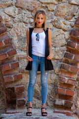 A beautiful woman  with long blond hair, a white blouse and blue jeaans  by the stone wall of the old town - image